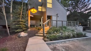 A modern two-story house with a visible staircase leading to the entrance, a well-maintained garden with rocks and plants, and a porch area with a lantern.