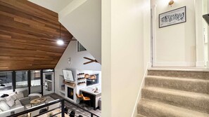 A modern interior with a wooden ceiling, a dining area with a fireplace, and a staircase with a framed picture.