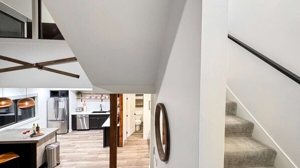 A modern kitchen with stainless steel appliances, a dining area with a bar stool, and a staircase leading to another level.