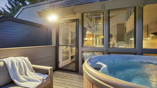 A hot tub with a glass enclosure, a wooden deck, and a view of the interior of a house.