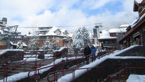 A snowy outdoor area with stone steps and railings, a ski lift, and buildings in the background.