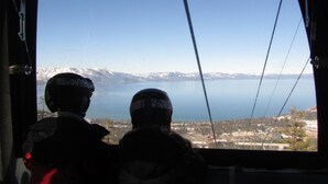 Two people in helmets looking out a window at a mountainous landscape with a body of water.