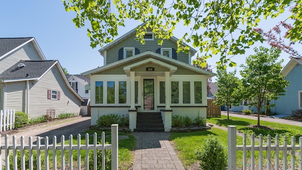 Une maison à deux étages avec un porche à l’avant, une allée et une clôture blanche en bois.