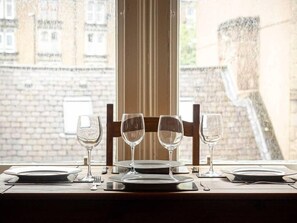 A table set for four with wine glasses and plates, positioned by a window overlooking a brick building.