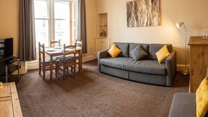 A living room with a grey sofa, wooden chairs, a TV, and a chandelier. - ☆ Central, Spacious Apartment Close to University☆ (Dundee)