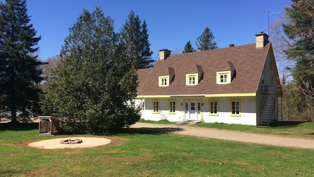A two-story house with a sloped roof, a chimney, and a front yard with a fire pit. - Villa st-Léon (Saint-Gabriel-de-Valcartier)
