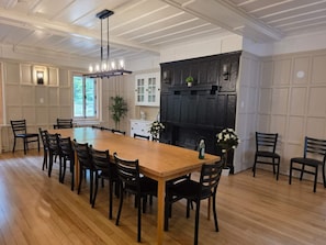 A dining area with a long wooden table and chairs, a chandelier, and a fireplace.
