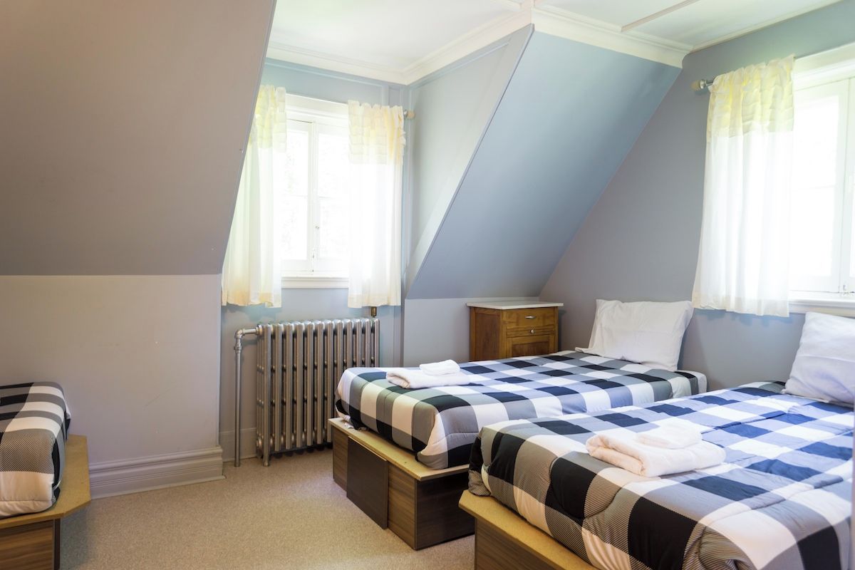 A bedroom with two beds, a radiator, a wooden nightstand, and a window with curtains.