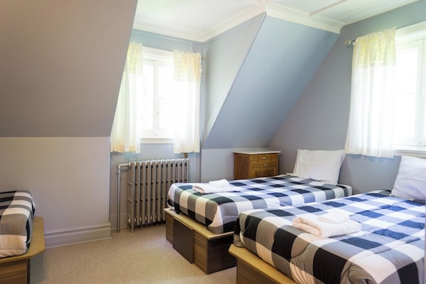 A bedroom with two beds, a radiator, a wooden nightstand, and a window with curtains.