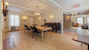 A spacious room with a large wooden table, multiple chairs, a chandelier, and a sign indicating a departure area. - Villa st-Léon (Saint-Gabriel-de-Valcartier)