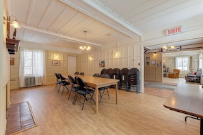 A spacious room with a large wooden table, multiple chairs, a chandelier, and a sign indicating a departure area. - Villa st-Léon (Saint-Gabriel-de-Valcartier)