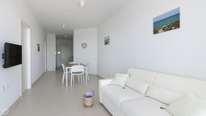 A modern, well-lit living room with a white sofa, a dining table with chairs, and a flat-screen TV mounted on the wall. - Rivazzurra Homes - 31 (Termoli)