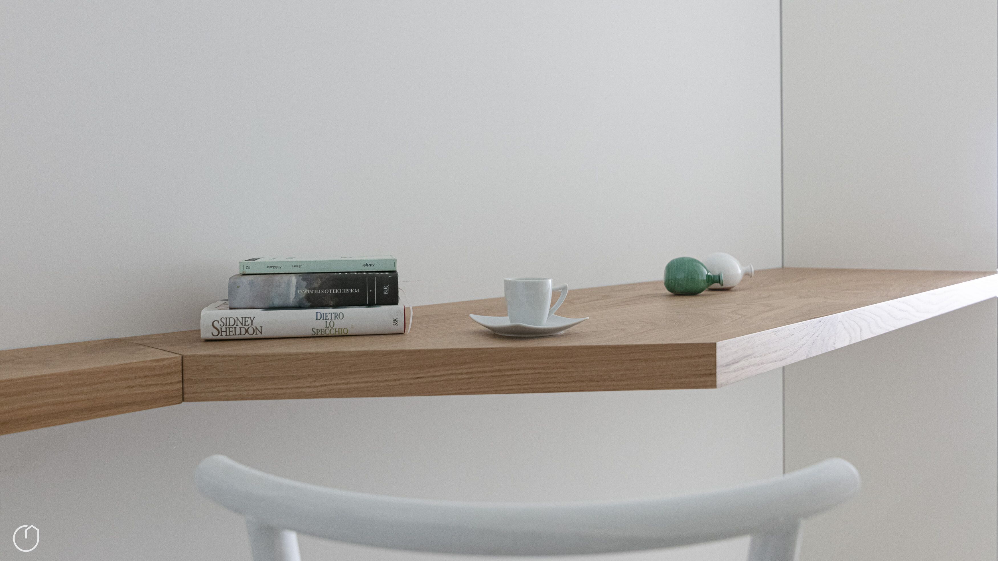 Une table minimaliste sur laquelle se trouvent une pile de livres, une tasse blanche et un objet vert, le tout posé sur une surface en bois.