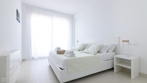 A minimalist white bedroom with a large bed, a bedside table, and a nightstand. - Rivazzurra Homes - 31 (Termoli)
