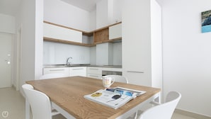 A modern kitchen with white cabinets and wooden beams, a dining table with chairs, and a magazine on the table.