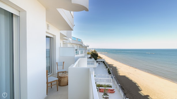 A beachfront balcony with a view of the sea, a wooden chair, and a small table.