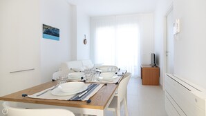 A modern, well-lit dining area with a wooden table set for four, white chairs, and a white sofa in the background.