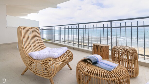 A balcony with wicker furniture, including a chair and ottoman, overlooking a beach with a metal railing. - Rivazzurra Homes - 7 (Termoli)