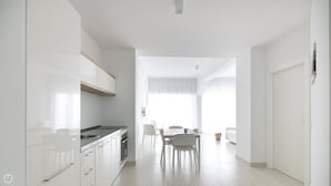 A modern kitchen with white cabinets, a stainless steel sink, and a dining area with a table and chairs. - Rivazzurra Homes - 7 (Termoli)