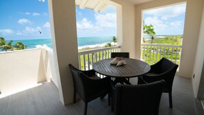 A balcony with a view of the ocean, a round table with chairs, and a pair of shoes on the table. - Secluded Retreat, Unbelievable Ocean View, Beach Front (Providenciales)