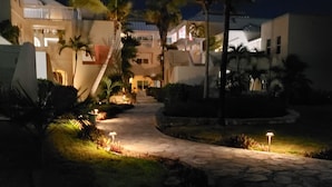 A nighttime view of a hotel courtyard with a paved walkway, palm trees, and illuminated outdoor lighting. - Secluded Retreat, Unbelievable Ocean View, Beach Front (Providenciales)