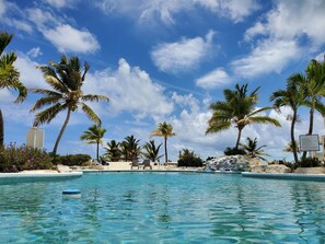 A pool area with palm trees, lounge chairs, and a clear blue sky. - Secluded Retreat, Unbelievable Ocean View, Beach Front (Providenciales)