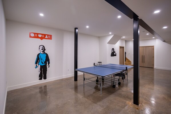 A spacious room with a ping pong table, a staircase, and a door leading to another area.