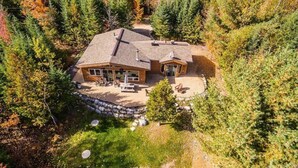 Una cabaña con una amplia terraza, un muro de contención de piedra y un fondo de bosque.
