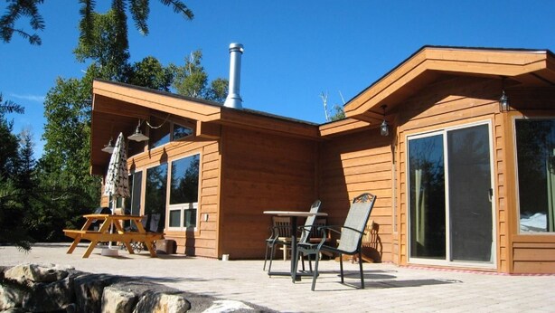 Una cabaña de madera con un área de patio, que incluye una mesa y sillas, y grandes puertas corredizas de vidrio.
