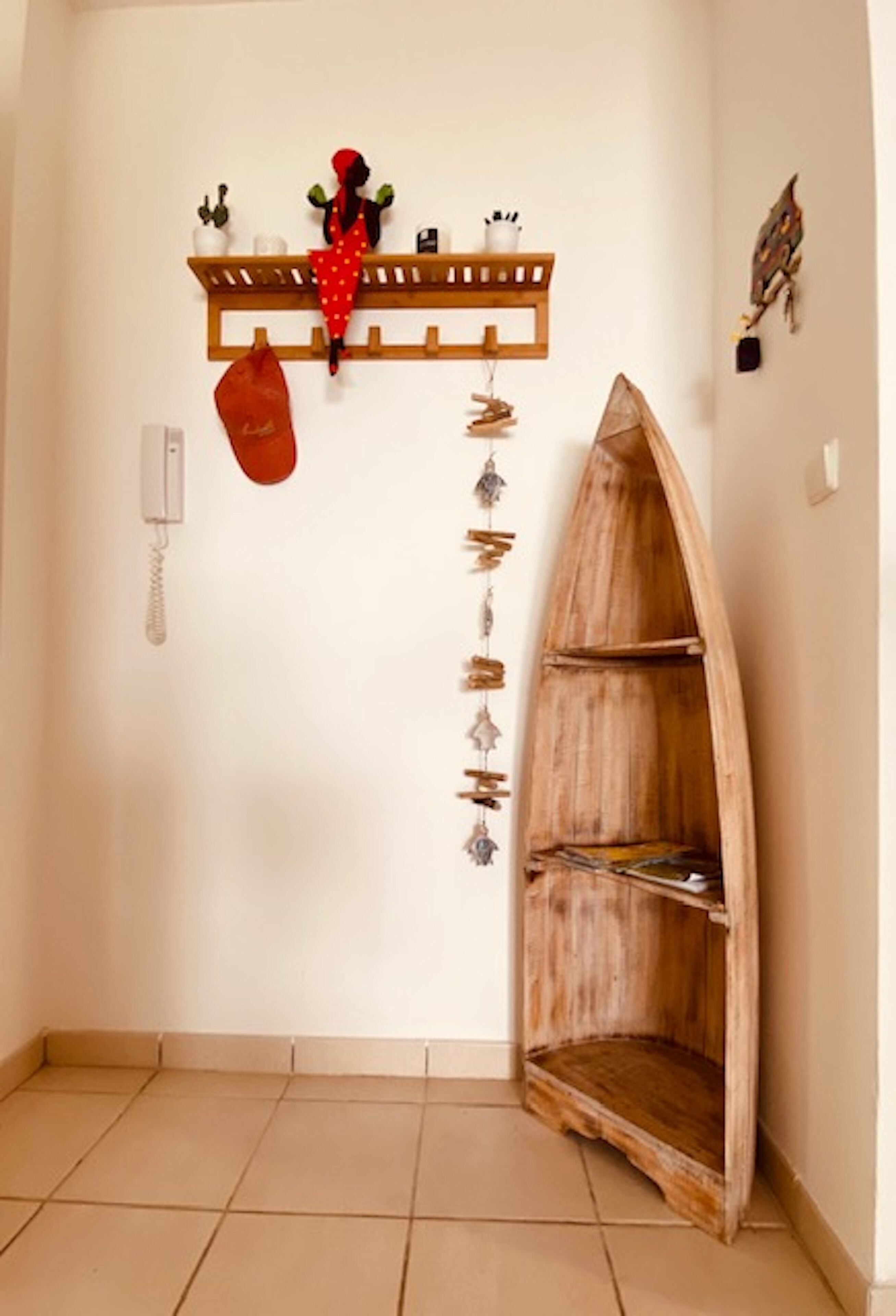 A corner of a room with a wooden shelf holding decorative items, a hanging red bag, and a wooden boat-shaped shelf.