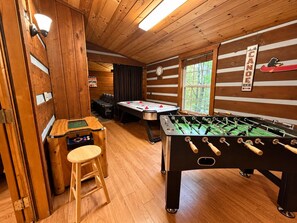 A cozy indoor space with wooden walls, a foosball table, a pool table, and a sign indicating a canoe rental service.