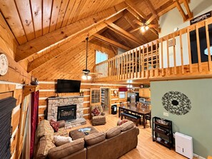 L’intérieur d’une cabane en rondins, avec une cheminée en pierre, un canapé, une table à manger et un balcon.