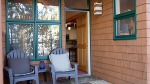 Une cabane en bois avec une véranda, deux fauteuils Adirondack et une porte donnant sur un coin cuisine.