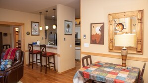 Un coin repas avec une table dressée pour deux personnes, un canapé et une cuisine en arrière-plan.