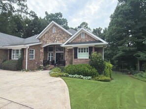 A two-story house with a stone facade, a front porch with a railing, and a well-maintained lawn. - Ultimate Getaway Minutes To Sanford Stadium. Fire Pit, Outdoor Kitchen & a Gym! (Athens)