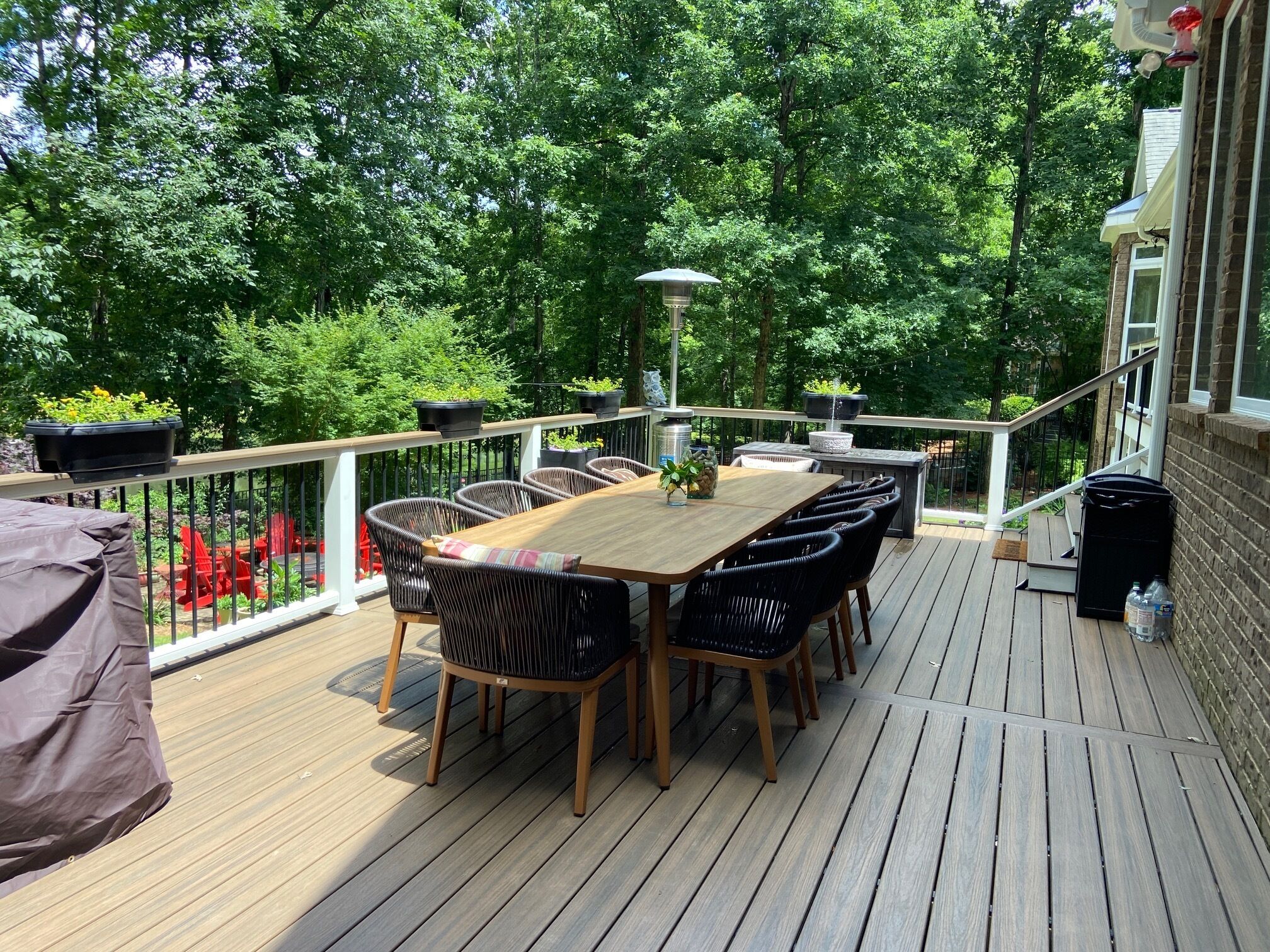 Een houten terras met een tafel en stoelen, omringd door potplanten en een balustrade.