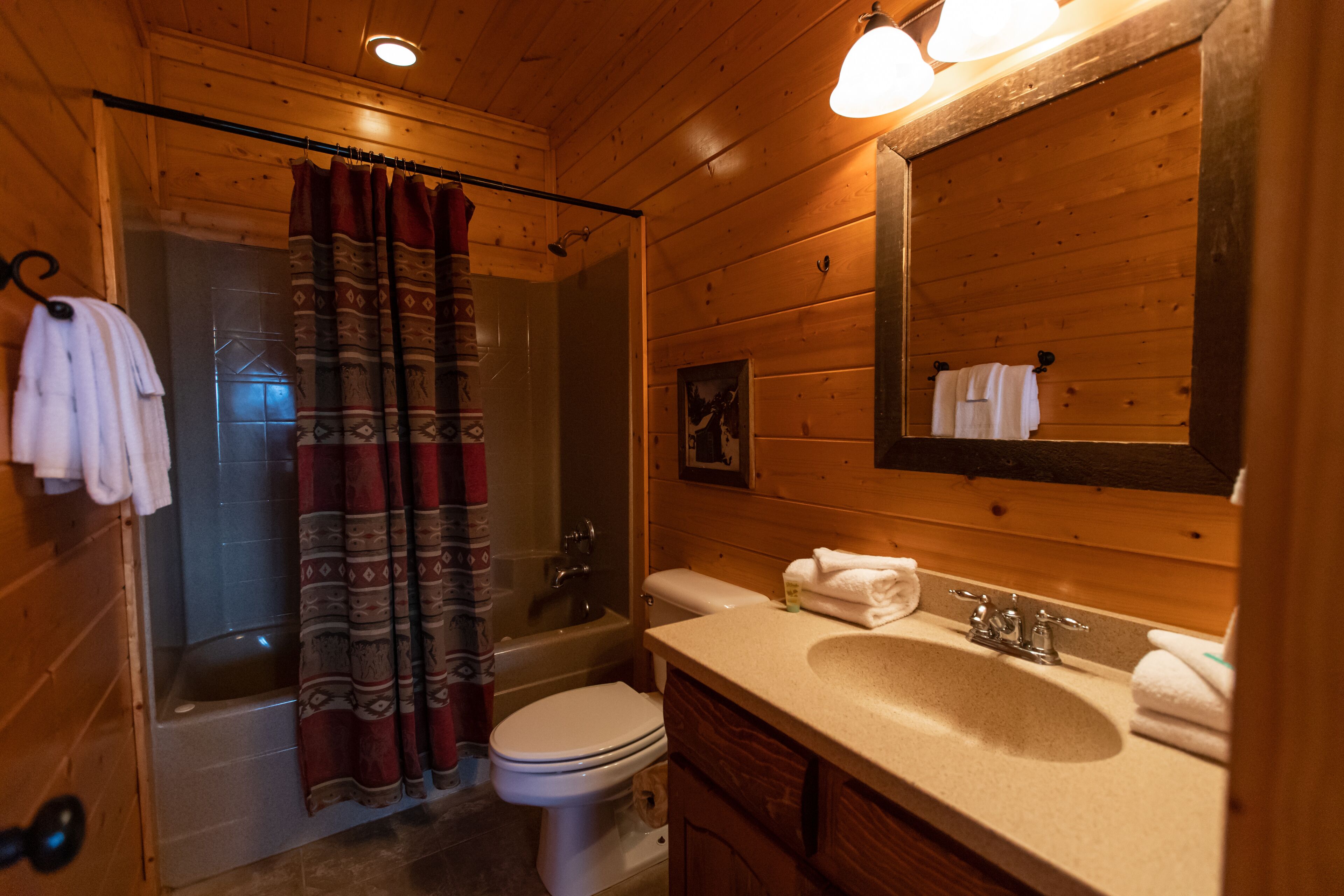 A wooden cabin bathroom with a shower, toilet, sink, and a large mirror.