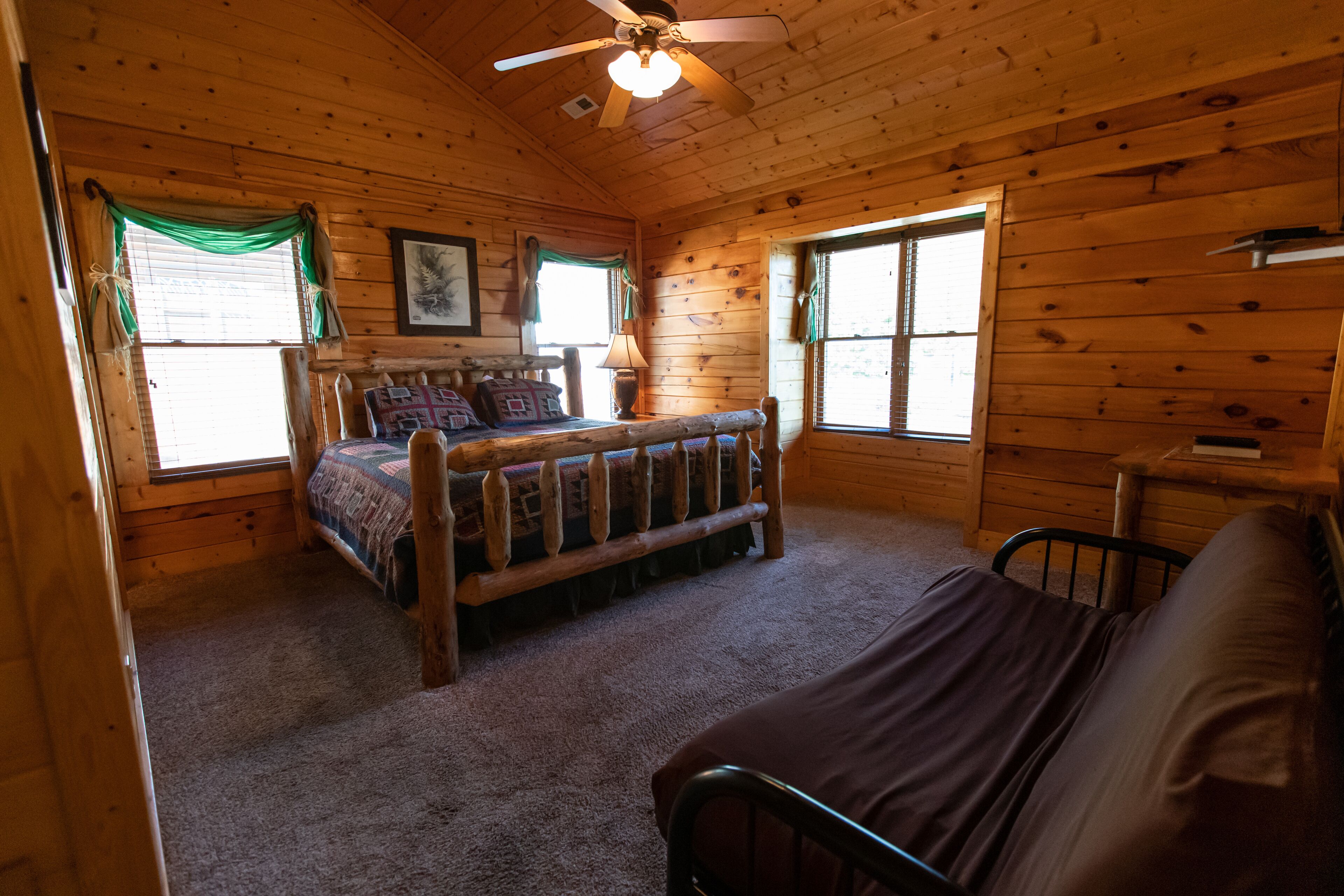 A wooden cabin bedroom with a bed, a bench, and a ceiling fan.