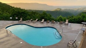 Una piscina con sillas de descanso y mesas, rodeada de exuberante vegetación y montañas al fondo.
