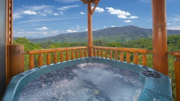 Un jacuzzi con terraza de madera y una vista panorámica de las montañas.