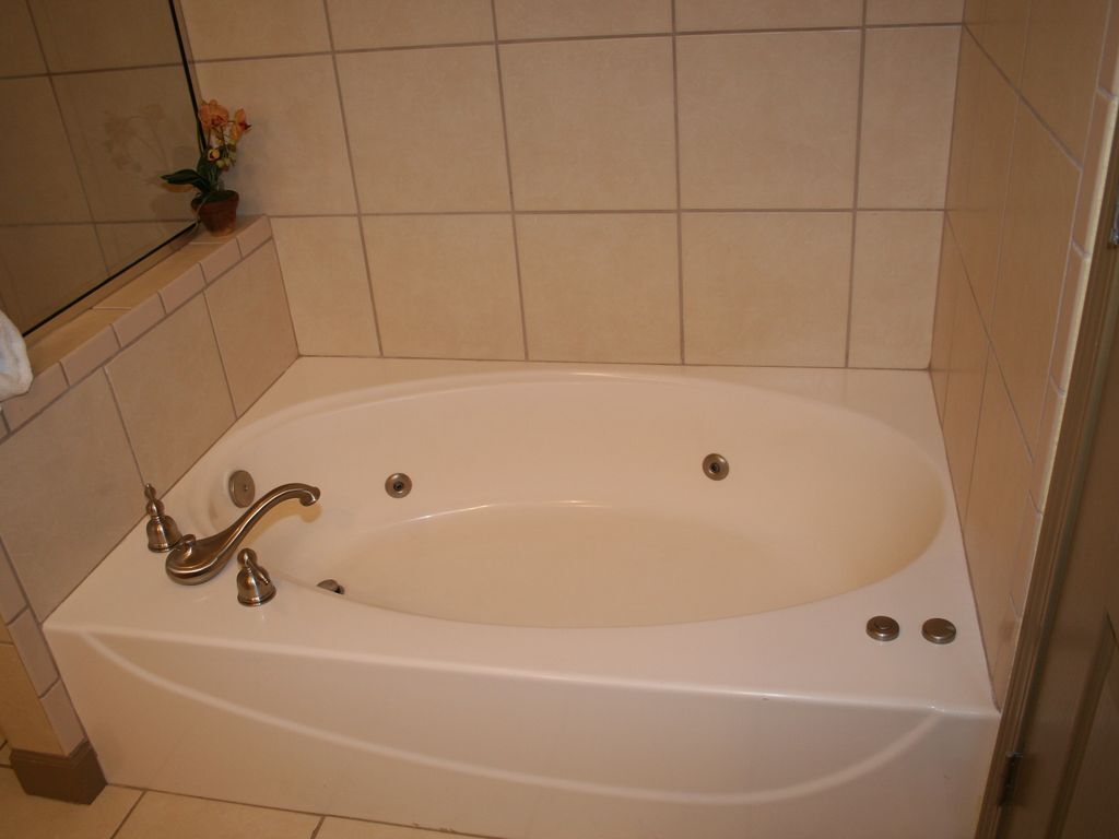 Eine weiße Badewanne mit einem Wasserhahn und zwei Abläufen, eingebaut in ein Badezimmer mit beige gefliesten Wänden und Boden.
