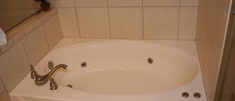 Eine weiße Badewanne mit einem Wasserhahn und zwei Abläufen, eingebaut in ein Badezimmer mit beige gefliesten Wänden und Boden.