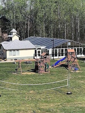 Un terrain de jeux avec des balançoires et des toboggans, un bâtiment équipé de panneaux solaires et une zone délimitée par une clôture.