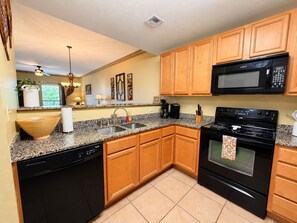 A kitchen with wooden cabinets, a black microwave, a stove, and a granite countertop.