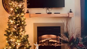 A living room with a Christmas tree, a flat-screen TV, a fireplace, and a mounted shelf. - Free Daily Activities - Beautiful Mountain Views - Indoor Pool (Pigeon Forge)