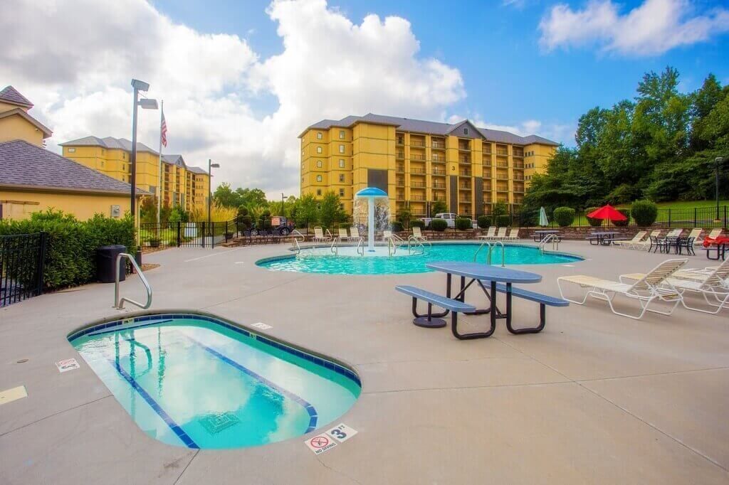 A hotel pool area with multiple pools, lounge chairs, and a water fountain.