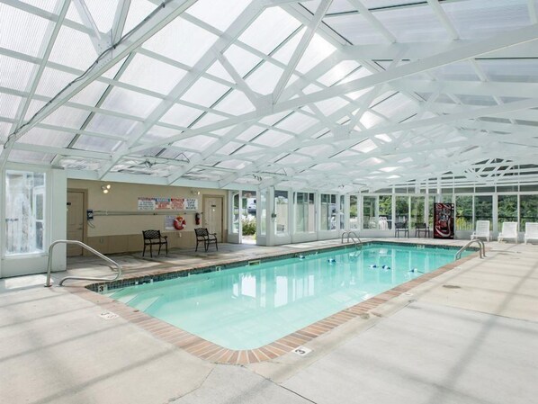 Una piscina interior con techo de vidrio, zona de la piscina despejada y algunas sillas de descanso.