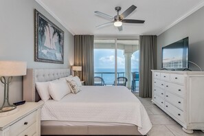 Une chambre d’hôtel avec un lit, une télévision, un ventilateur de plafond, un tableau et une vue sur la mer.