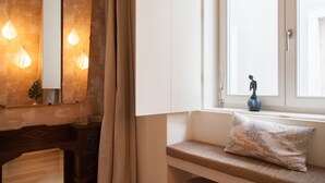 A room with a wooden bench, a white cabinet, a mirror, and a window with a view. - FLH Chiado Nature Apartment (Lisbon)