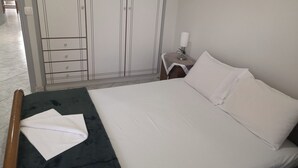 Un lit bien fait, avec du linge de lit blanc, dans une chambre qui comprend une armoire et une table de chevet avec une lampe.